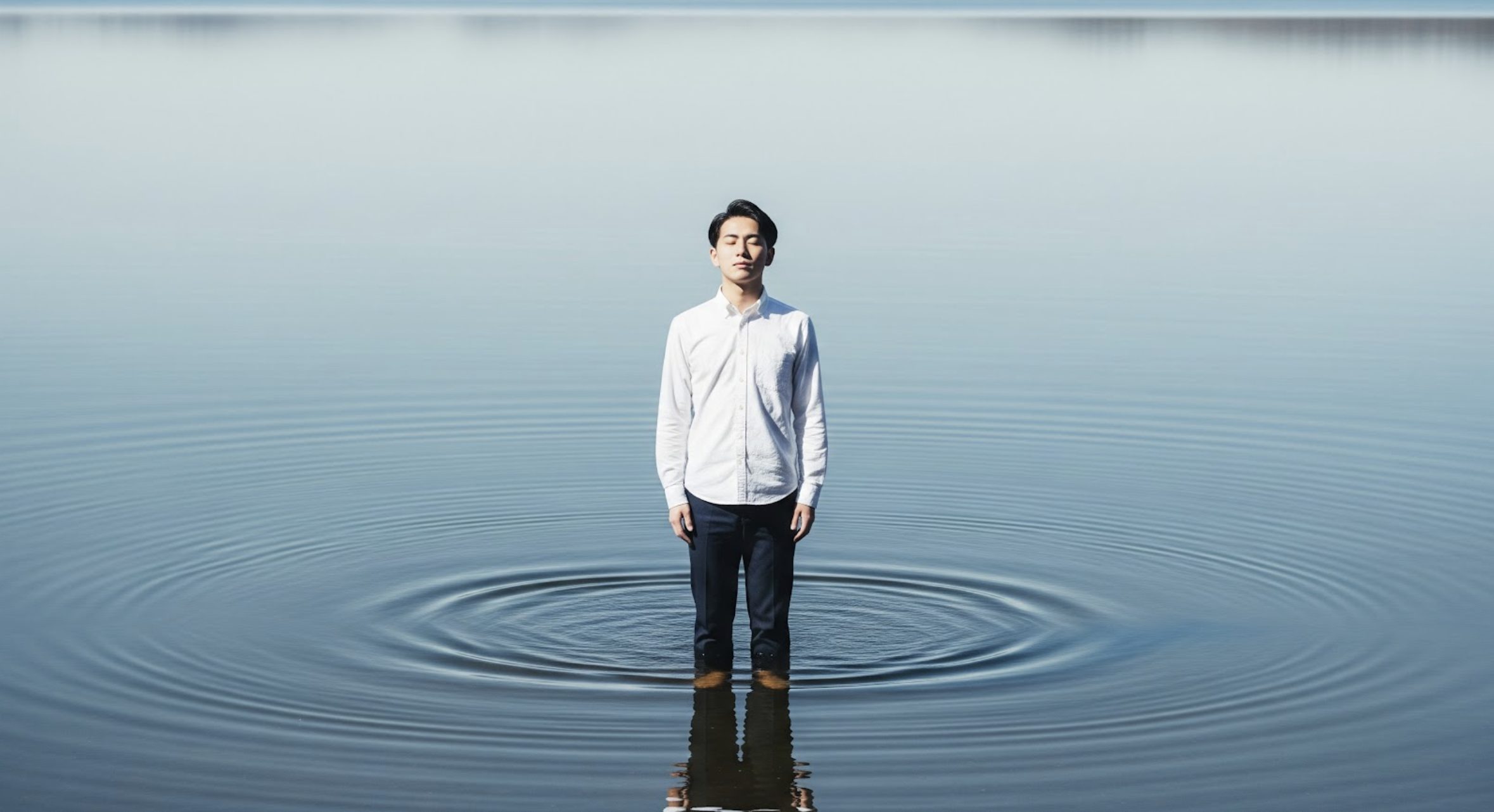 広大な、穏やかな湖の中央に立つ男性